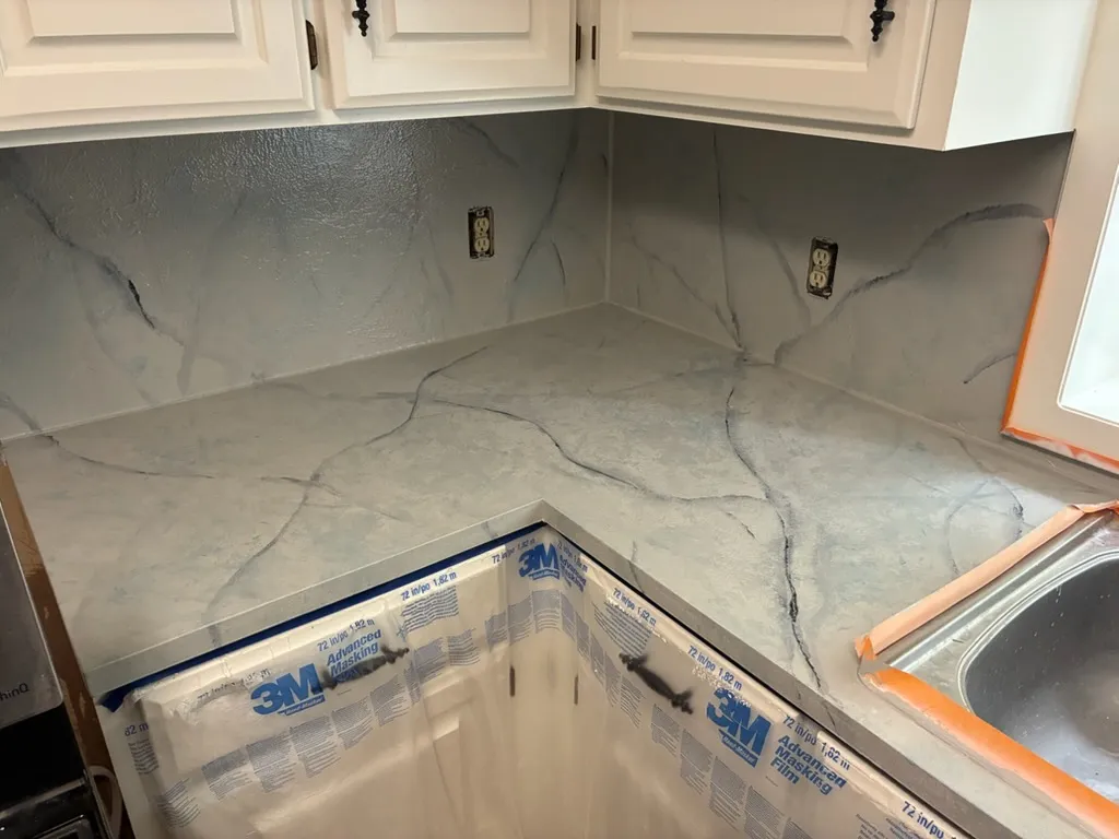 Corner countertop and backsplash with gray marble veining under white cabinets